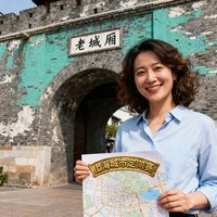 上海城市定向赛资深策划人赵女士半身照，手持定制地图站在上海老城厢古城门前，笑容自信从容